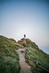 En person står på en bergsknall i slutet av en stig och tittar ut mot horisonten